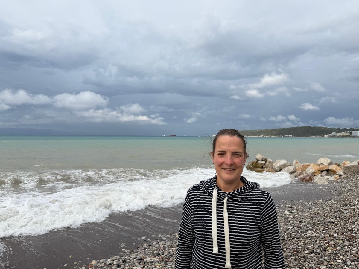 Suzan Heideman standing on a pebble beach with waves and a stormy sky behind her